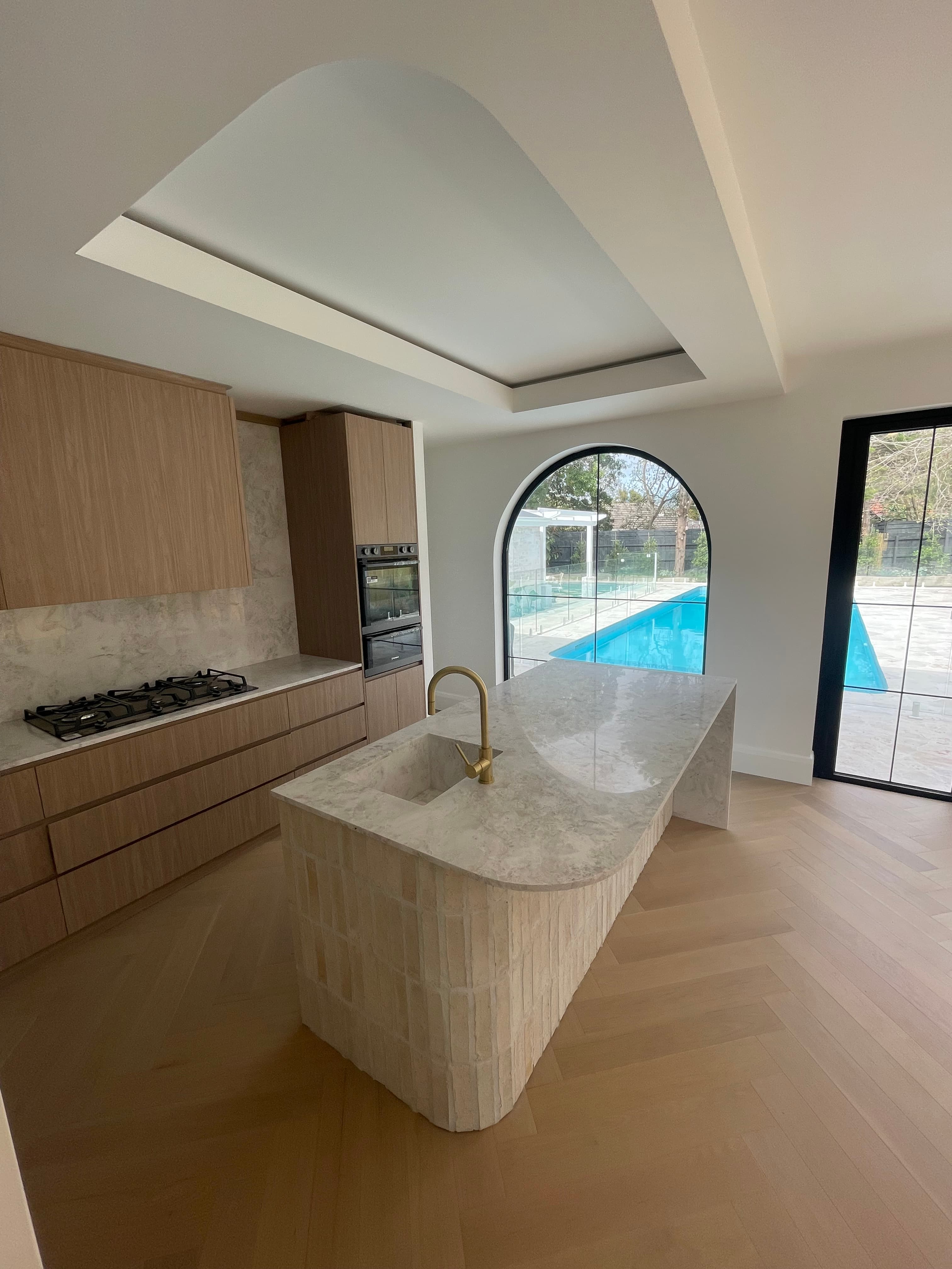 Completed kitchen featuring Chinese-sourced marble benchtops, timber cabinetry, and brass tapware